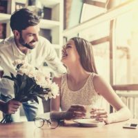 woman surprised by the flowers given by her boyfriend while waiting inside a cafe