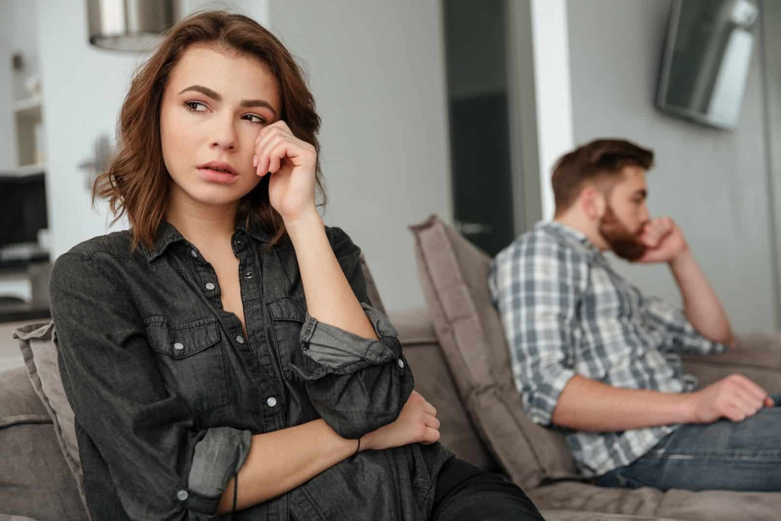 sad woman crying sitting at the end of the sofa with a silent guy on the end inside the living room