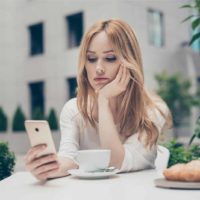 sad woman in white top looking at phone