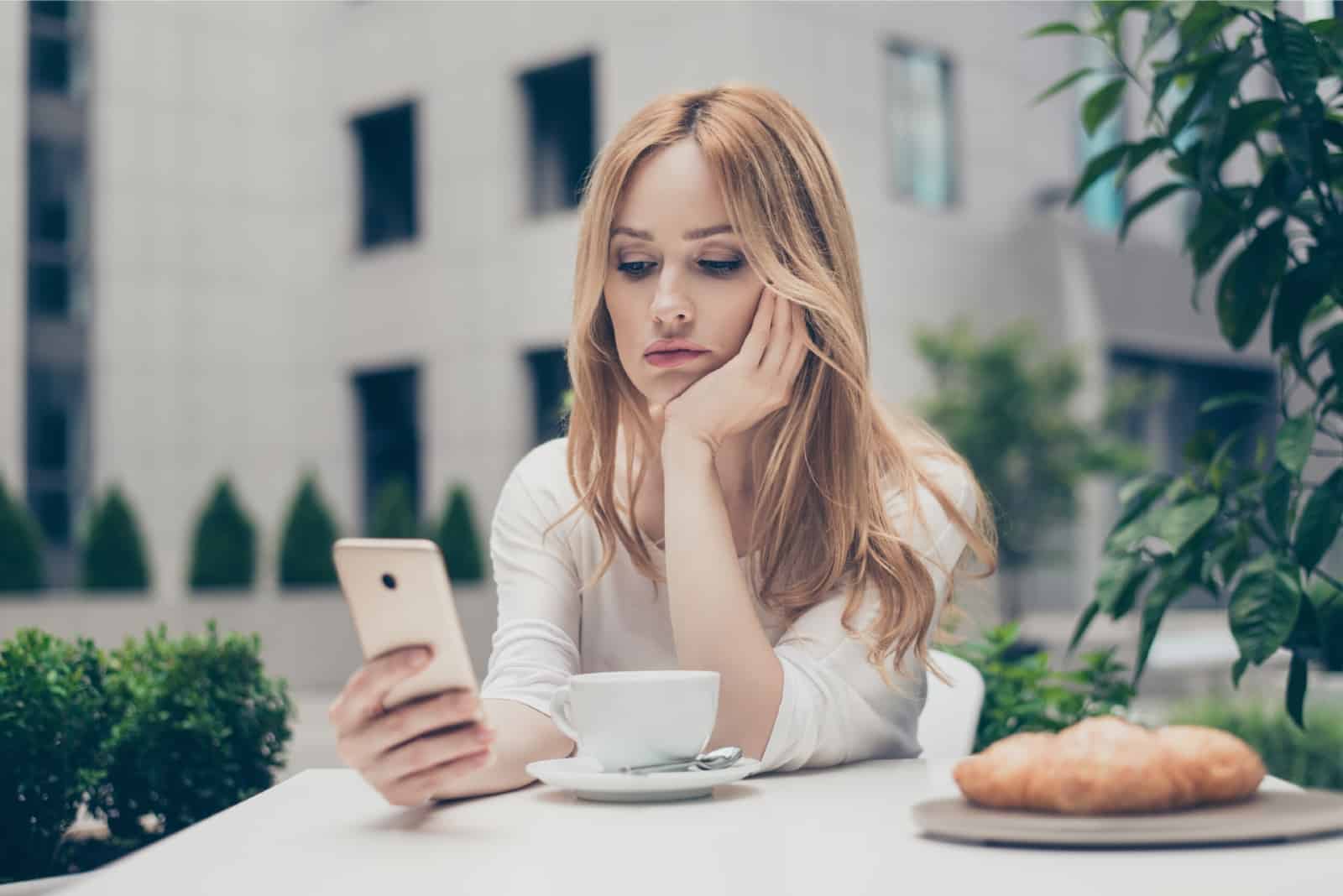 sad woman in white top looking at phone