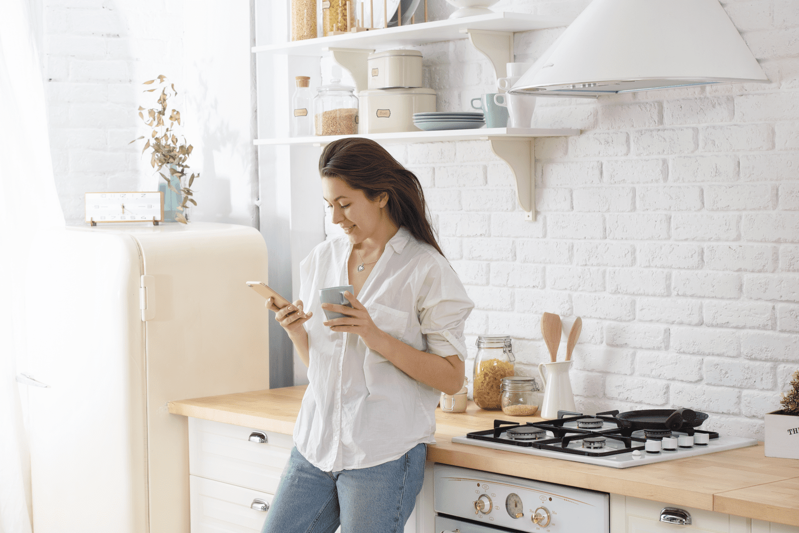 a smiling woman standing in the kitchen and buttoning the phone
