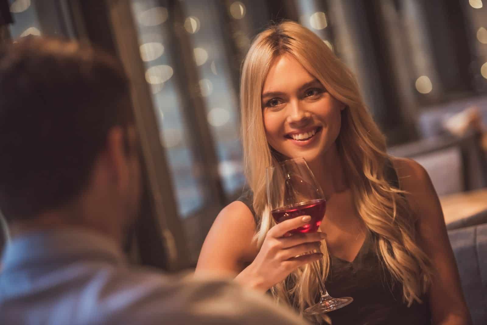 schöne junge Frau, die ihr Date mit einem Glas Wein betrachtet