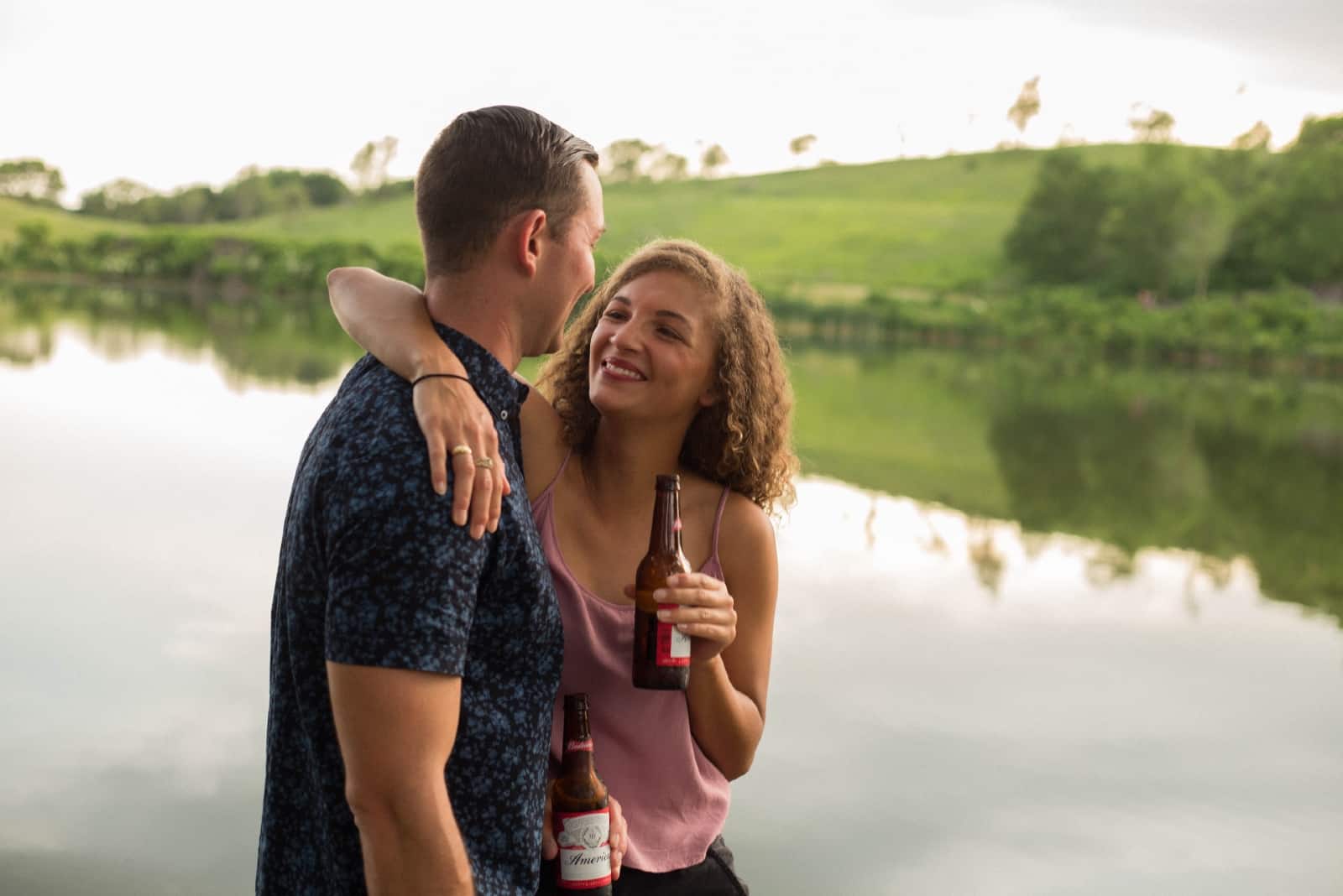 hombre y mujer felices bebiendo cerveza cerca del agua