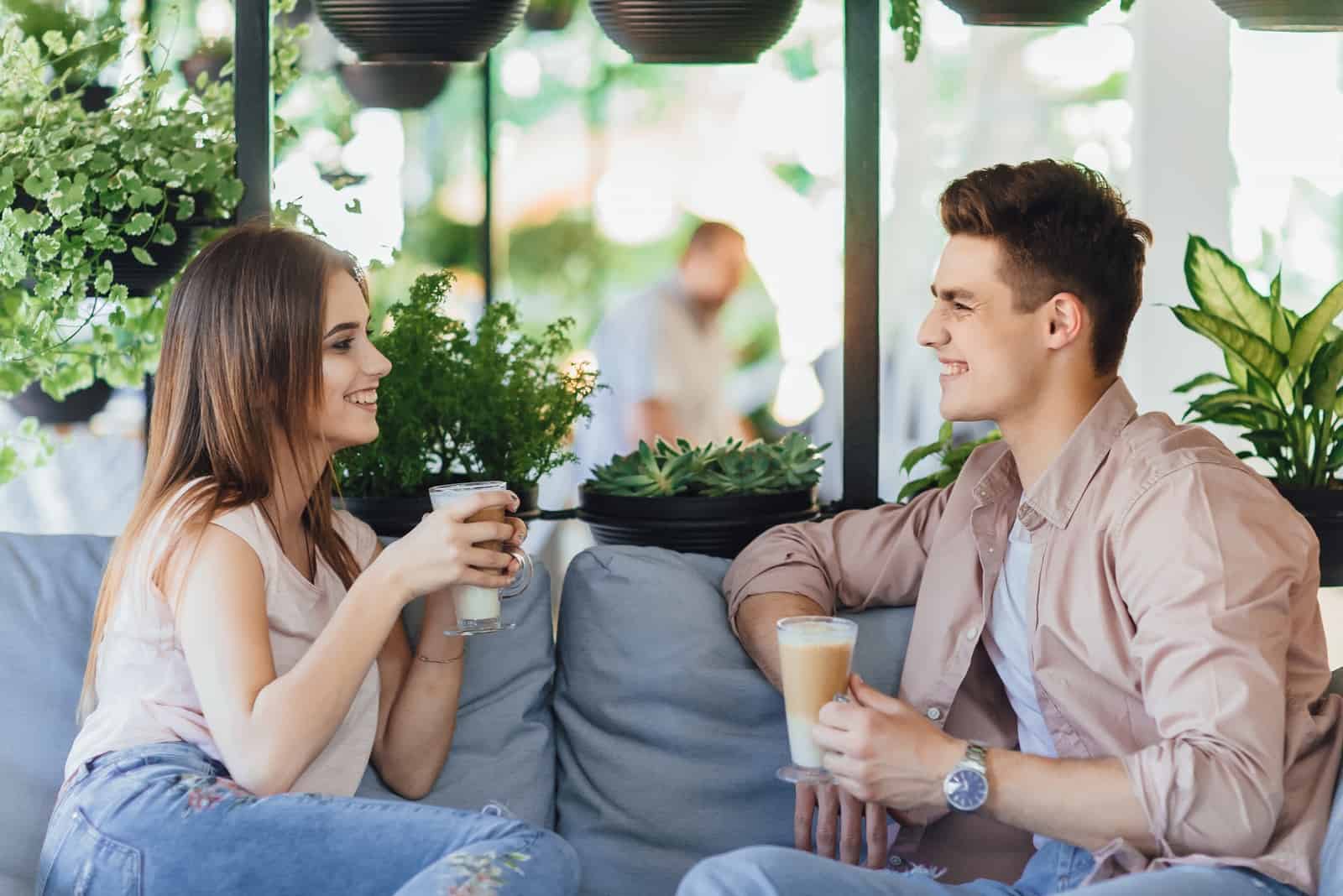 man and woman smiling while drinking coffee in cafe