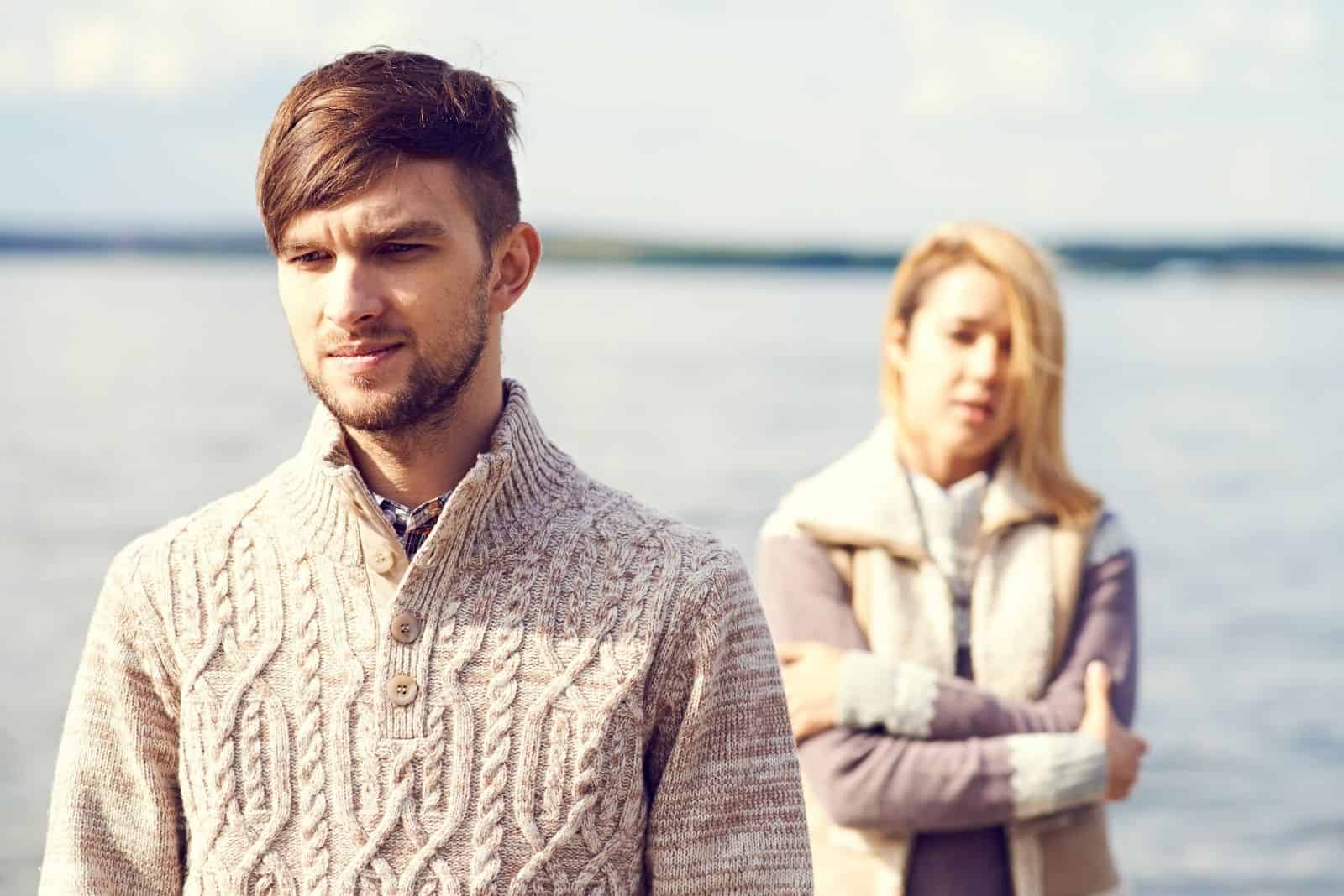 couple in conflict with the woman reaching out to the man standing near the sea