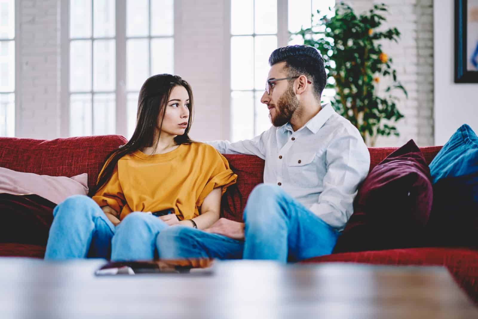 man and woman talking while sitting on sofa