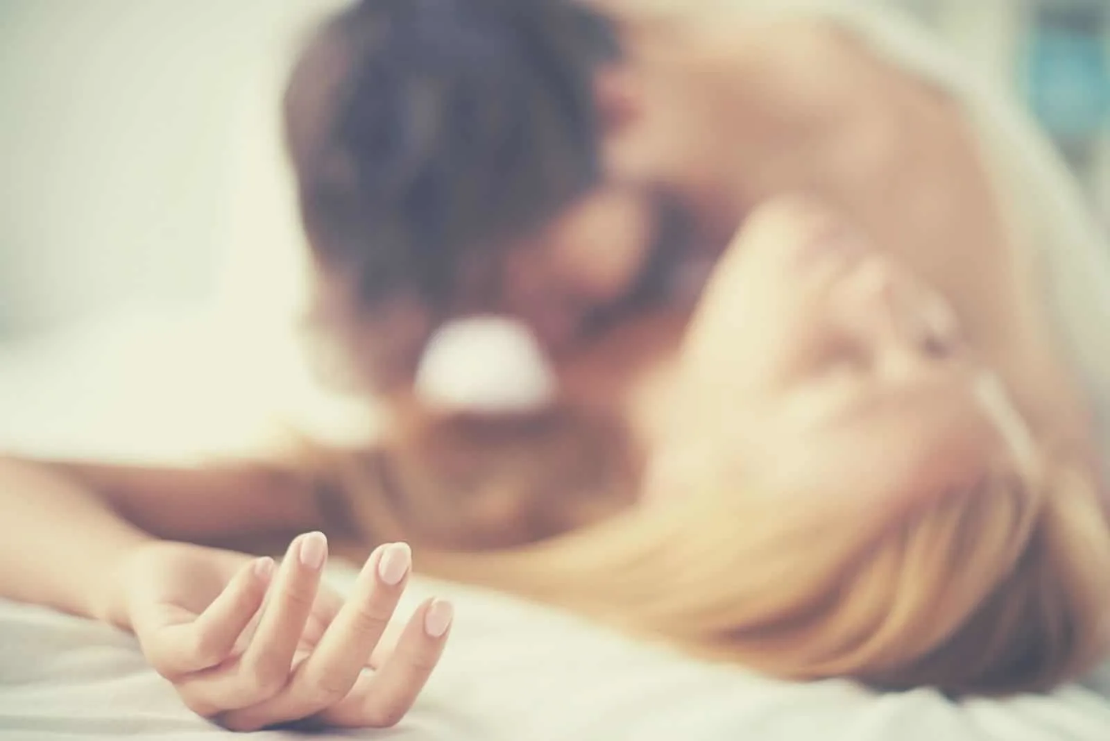 hand of a pleased woman in focus lying in bed while man carressing her