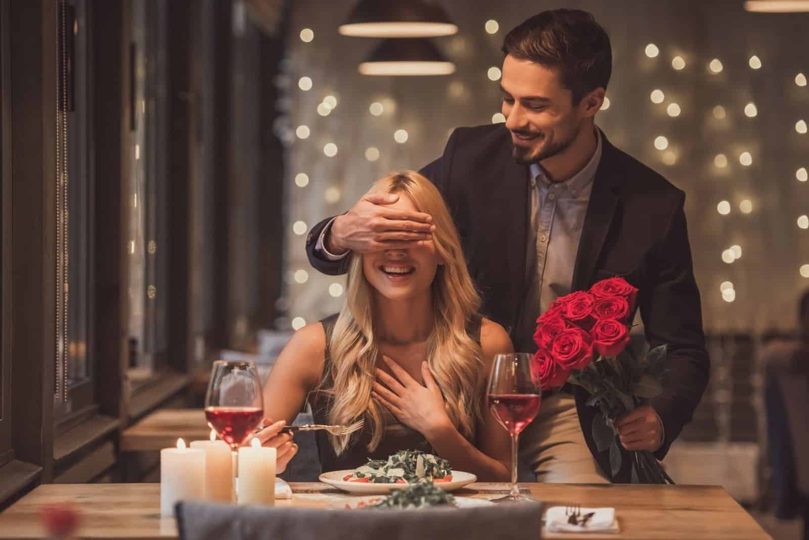 hübscher eleganter Mann, der Blumen bringt und seine Frau überrascht, die im Restaurant wartet