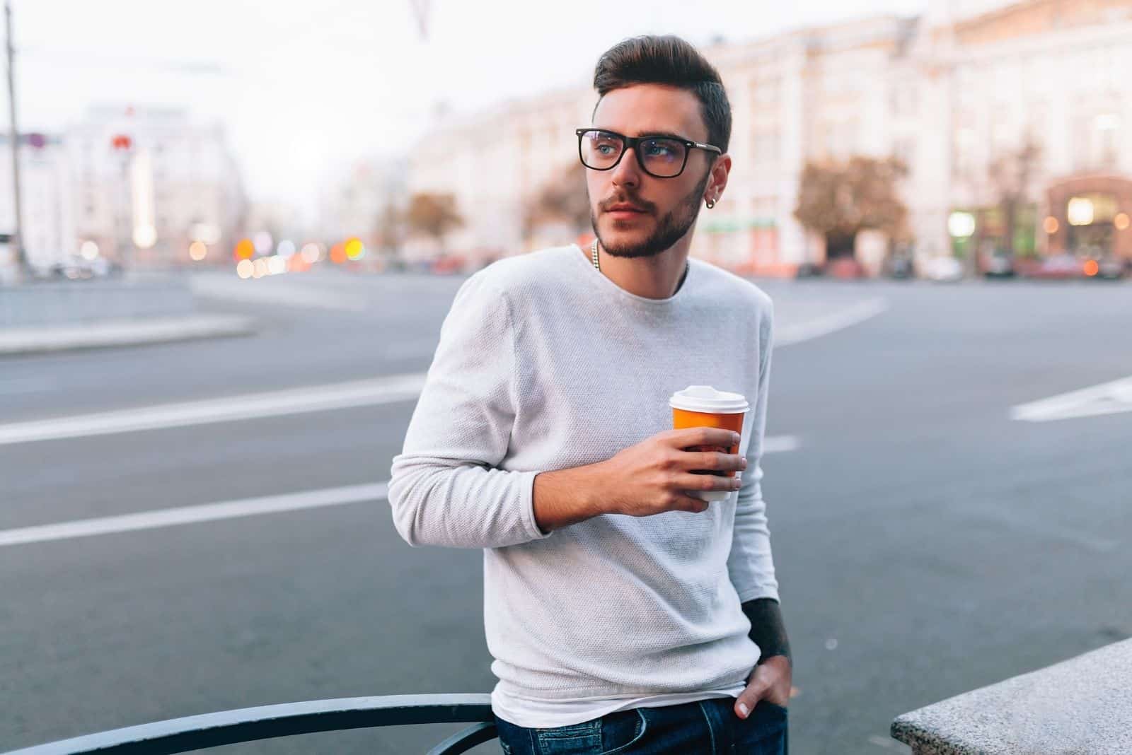 Hipster-Mann, der auf der Straße steht und eine Tasse Kaffee hält