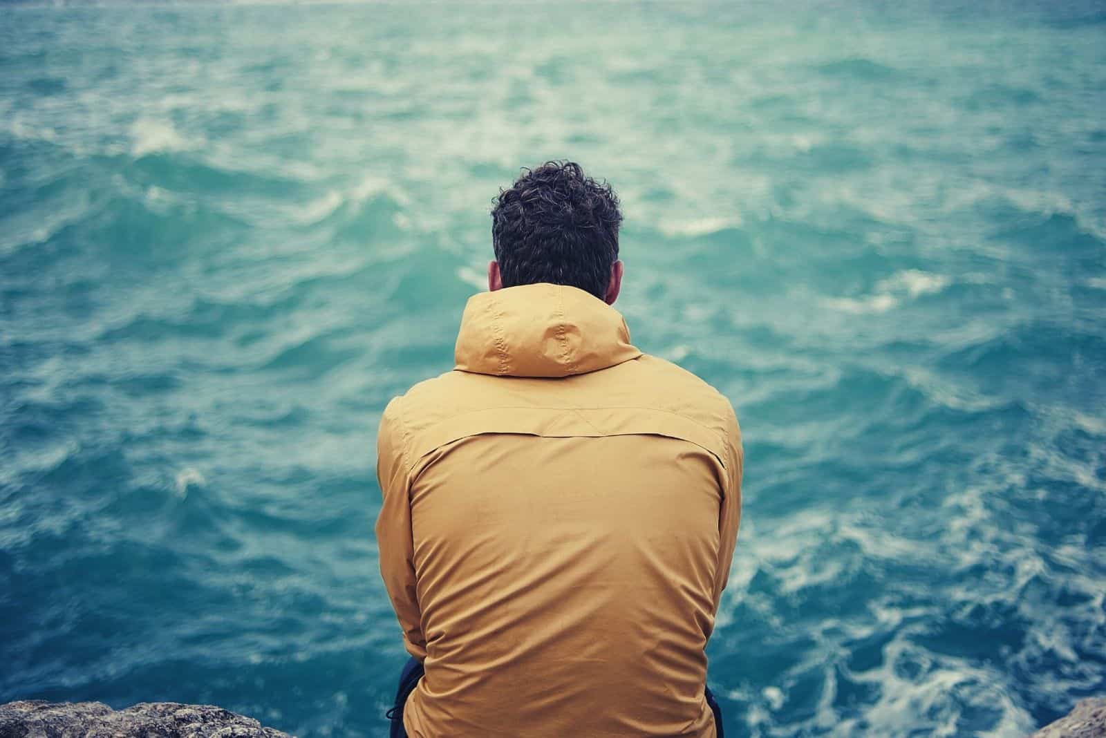 hombre solitario mirando al mar sentado en las rocas