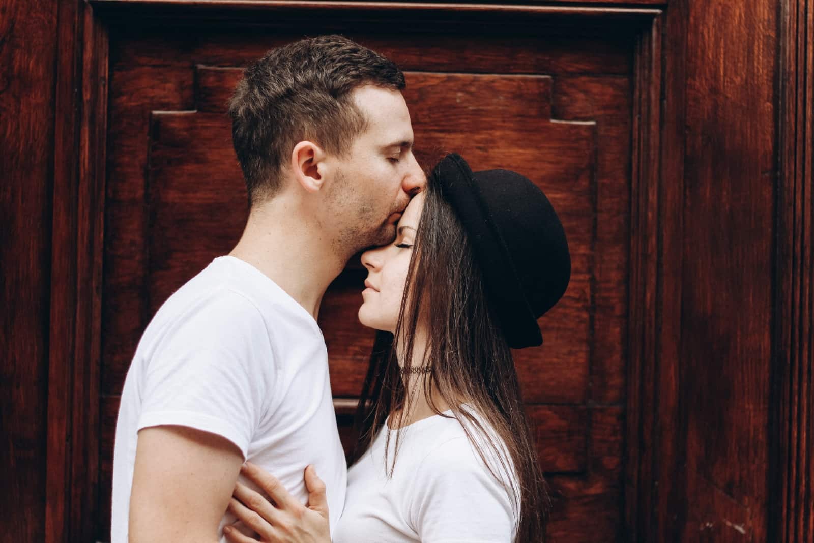 man in white t-shirt kissing woman's forehead