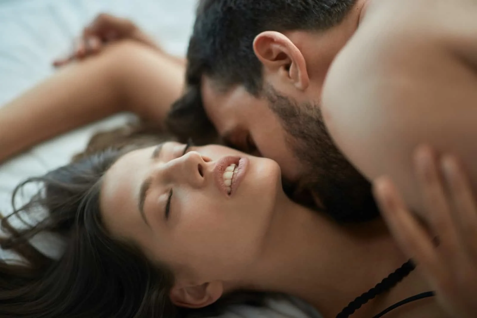 man kissing woman's neck while laying on bed