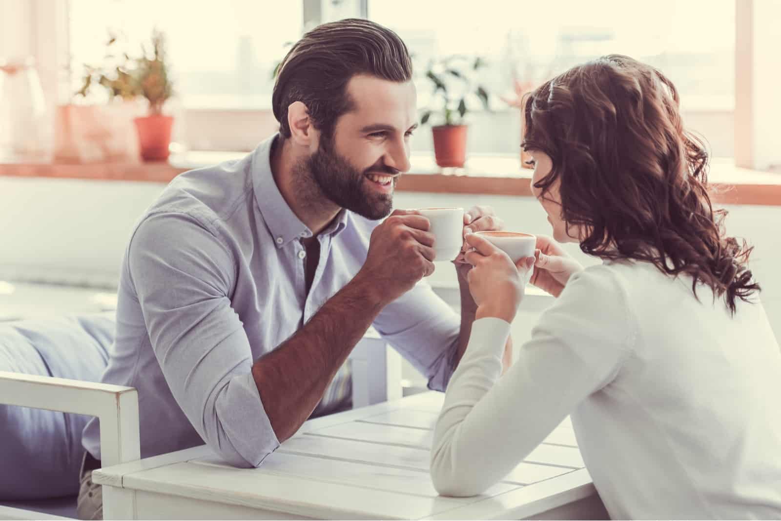 homem feliz a olhar para uma mulher enquanto está sentado num café