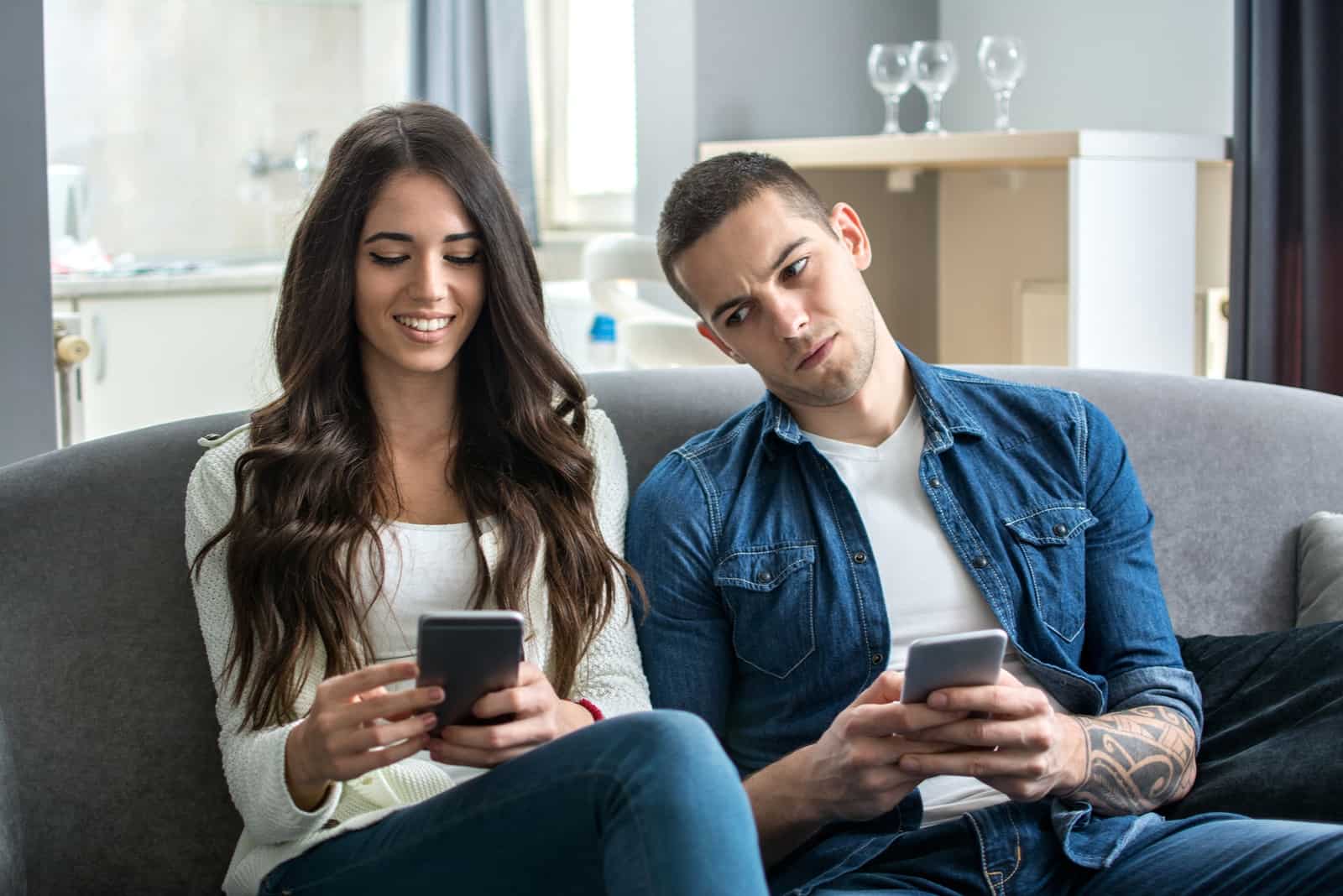 man looking at woman's smartphone while sitting on sofa