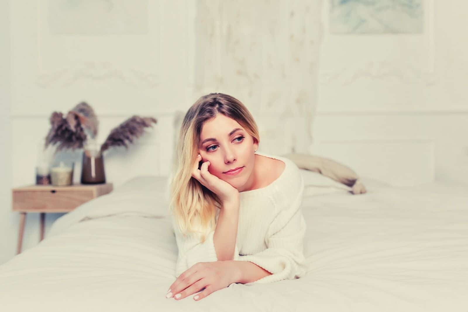 pensive woman lying in bed with one hand on her chin supporting the head