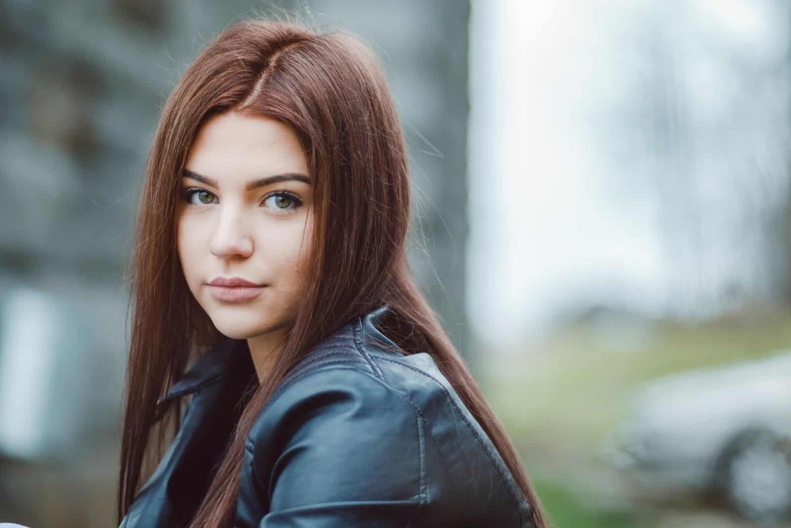 pretty young student looking at the camera wearing leather jacket sitting outdoors