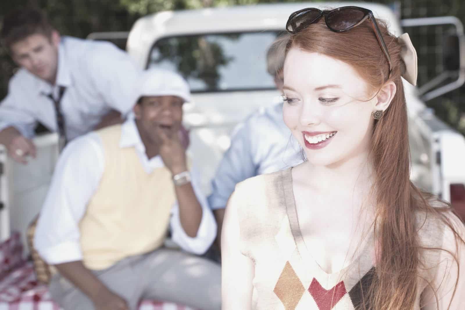 pretty young woman reacting to her suitors sitting at the truck in the background