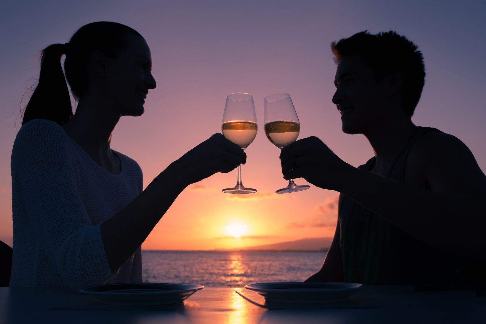 casal romântico a beber um copo de vinho durante um encontro junto à baía ao pôr do sol