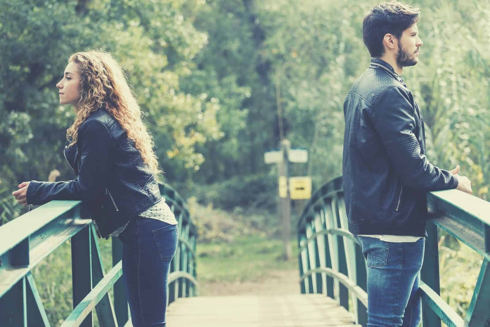 sad couple having conflict standing on the opposite side of the bridge 