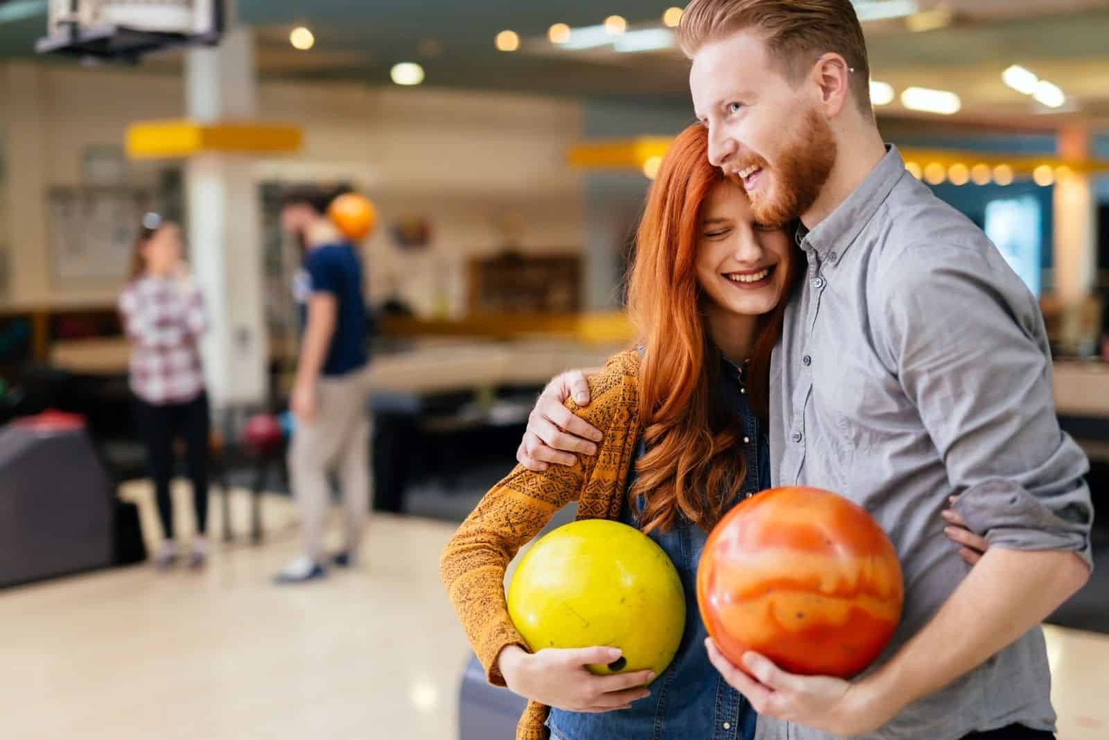  dulce pareja abrazándose dentro de una bolera sosteniendo una bola de bolos