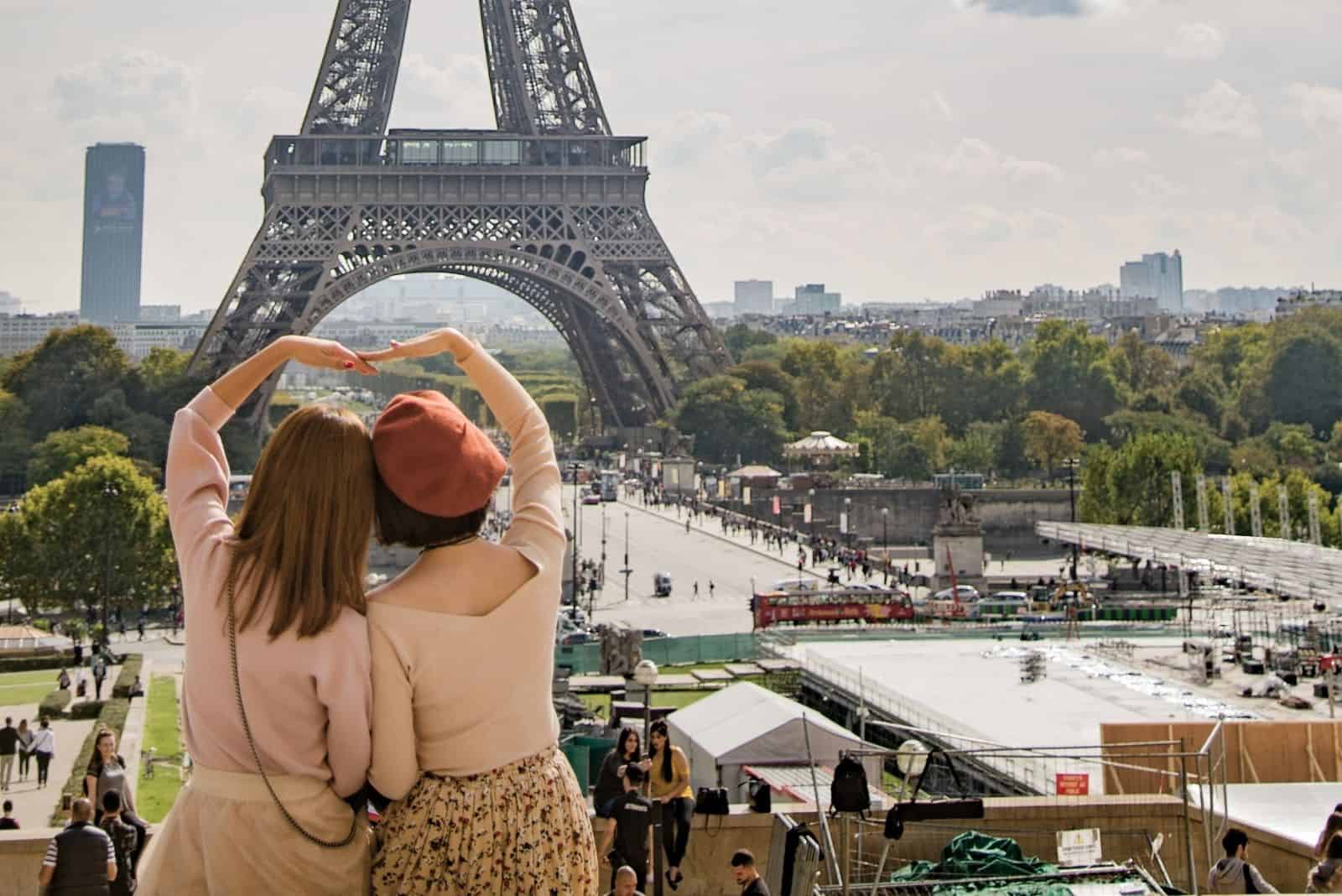 dos francesas haciendo un corazón con las manos frente a la torre Eiffel en Francia