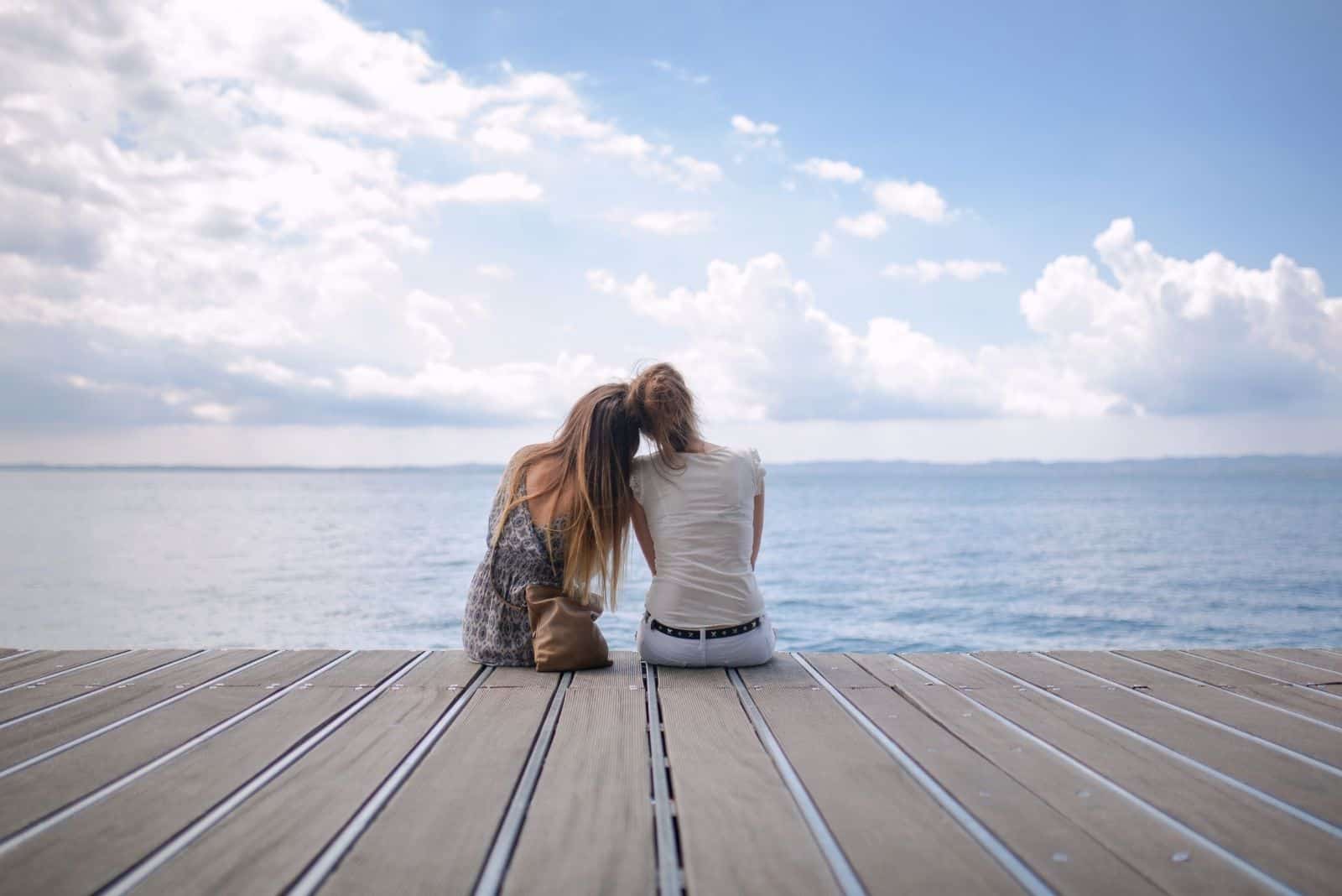 two friends sitting on a web in front of the sea leaning on each other looking at the beautiful view 