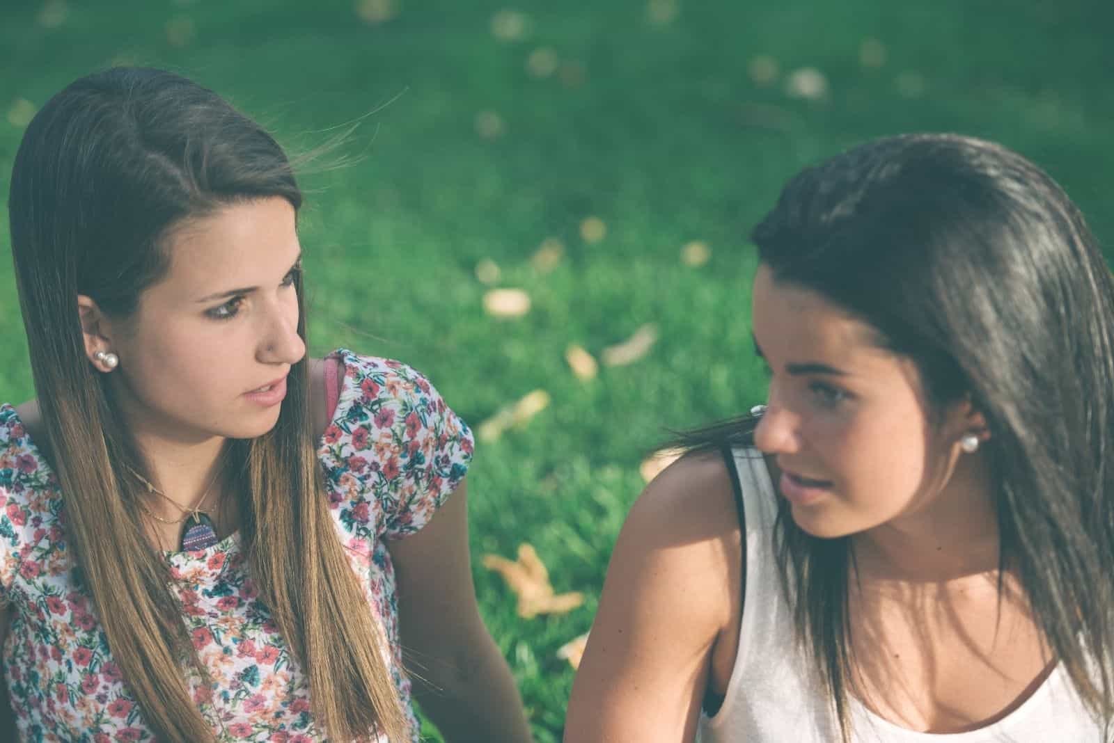 two young friends talking seriously outdoors sitting on the ground