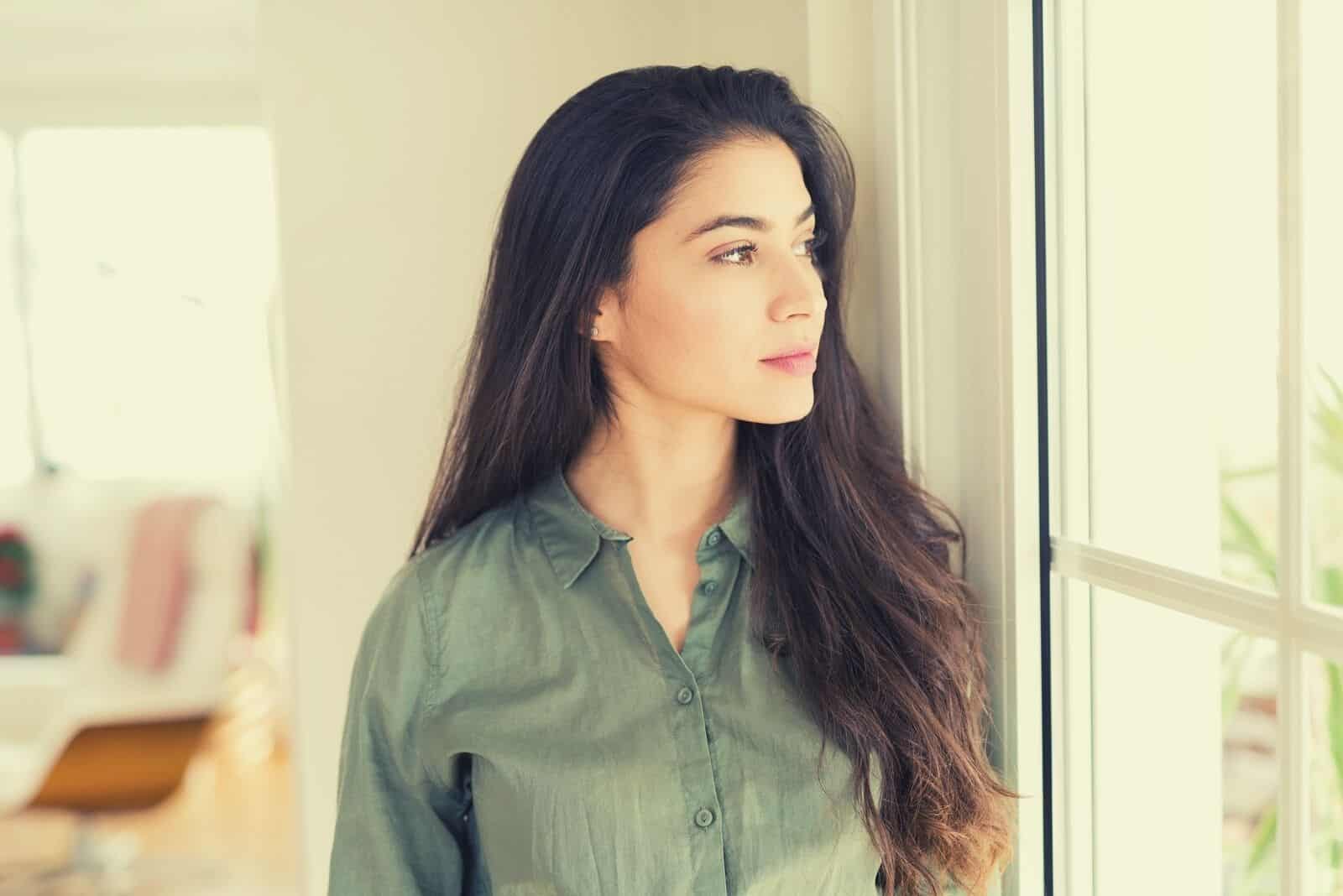 mujer profundamente pensativa mirando por la ventana de pie