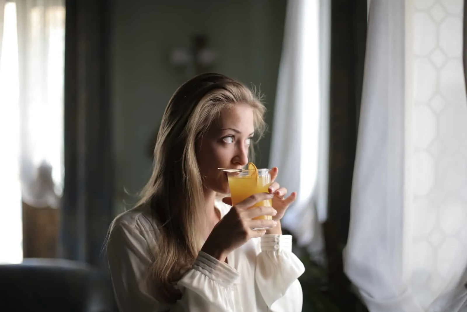 woman drinking orange juice while looking through window