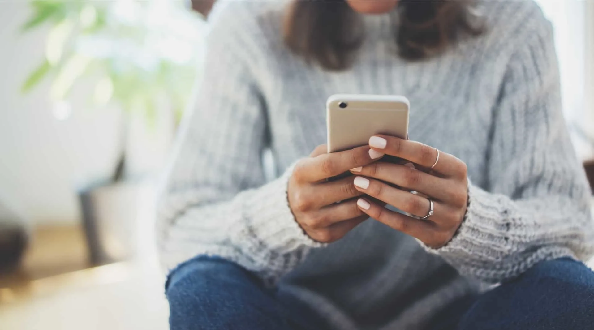 woman in gray sweater holding smartphone