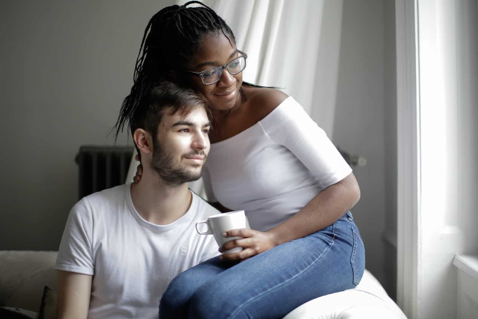 woman in white top hugging man while sitting on sofa