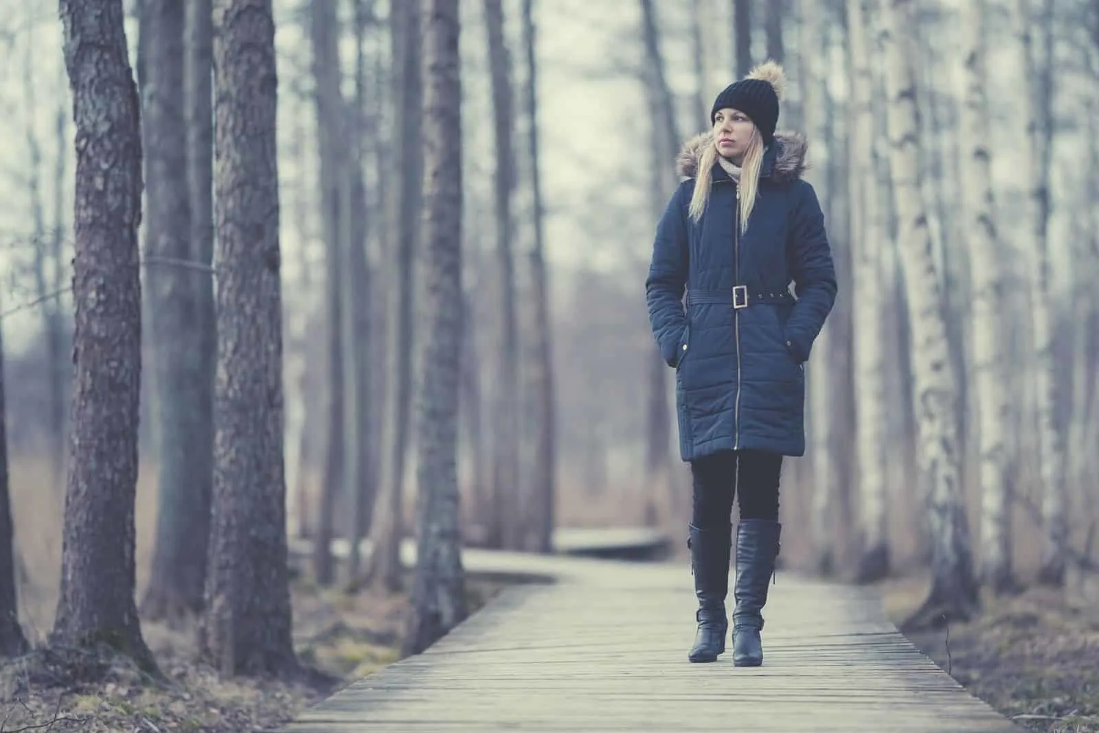 woman in winter clothes walking thru the pathway in the park with tall trees
