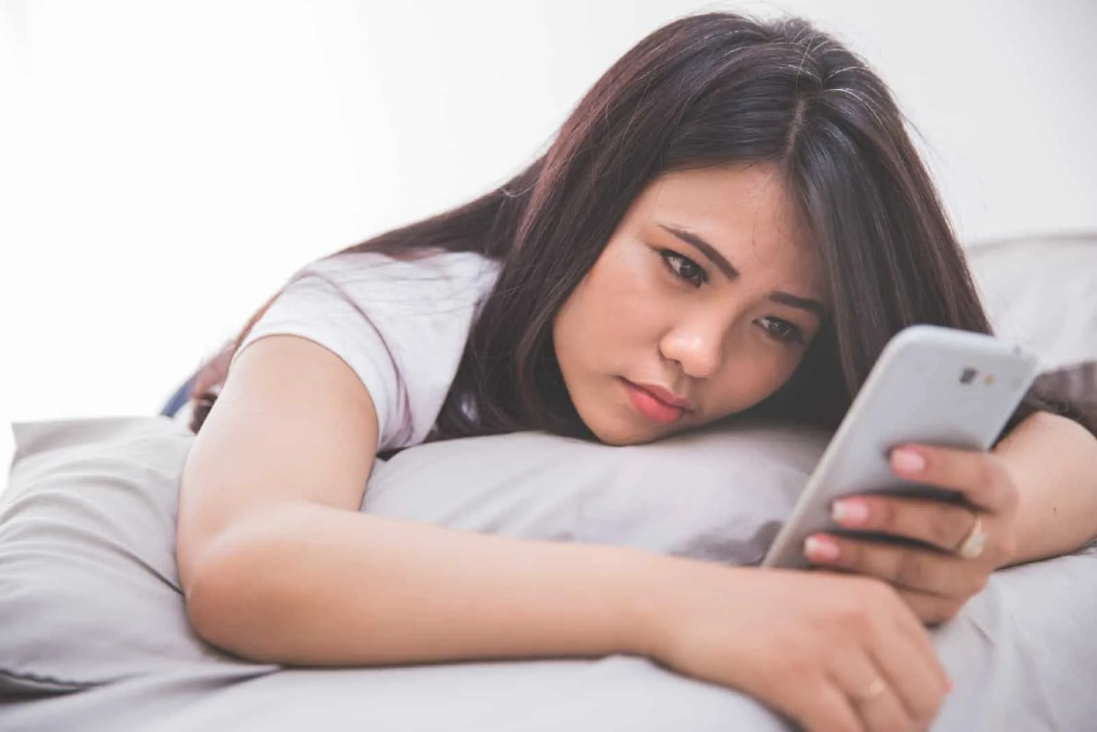 sad woman laying on bed while using smartphone