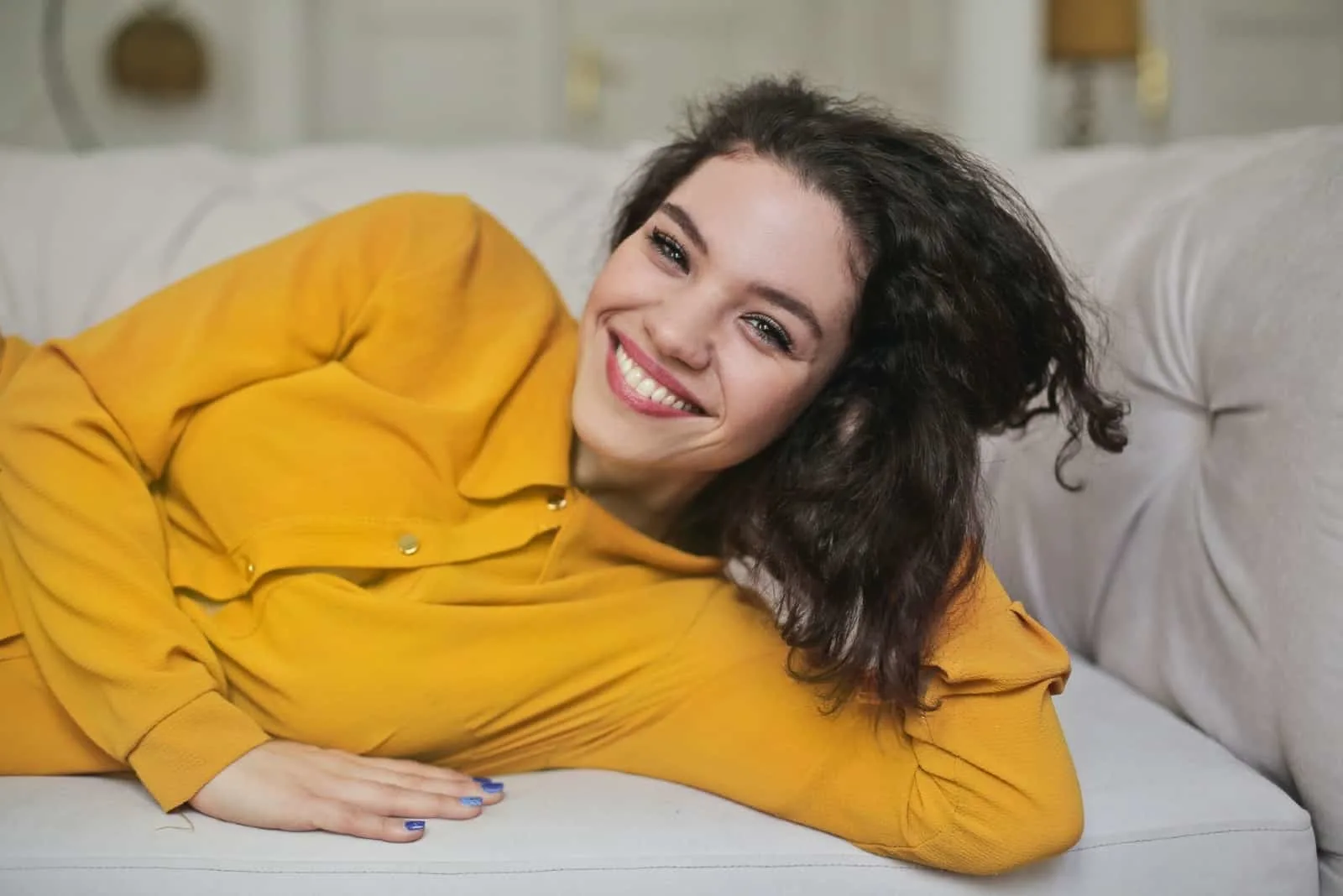 woman in yellow shirt smiling while laying on sofa