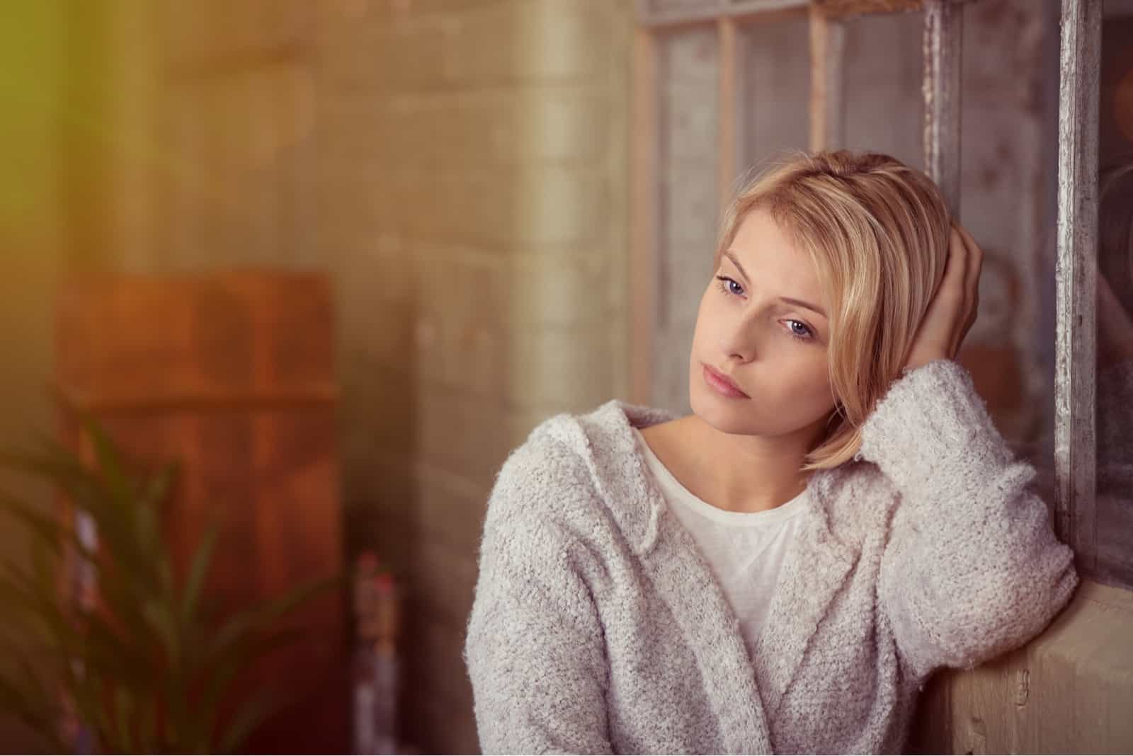 blonde woman in white cardigan leaning on wall