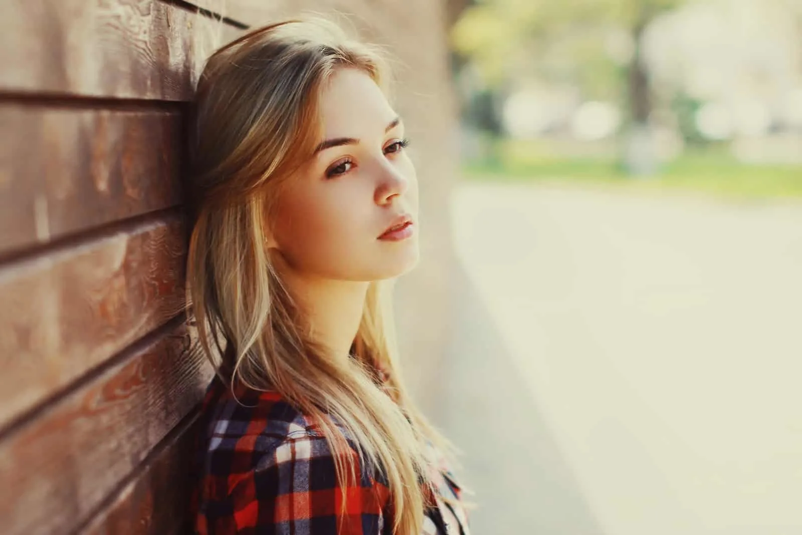 blonde woman in red checked shirt leaning wall