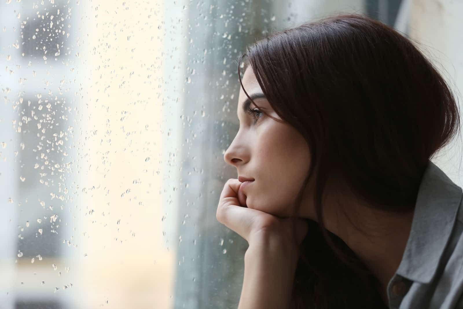 pensive woman looking through window during rainy day