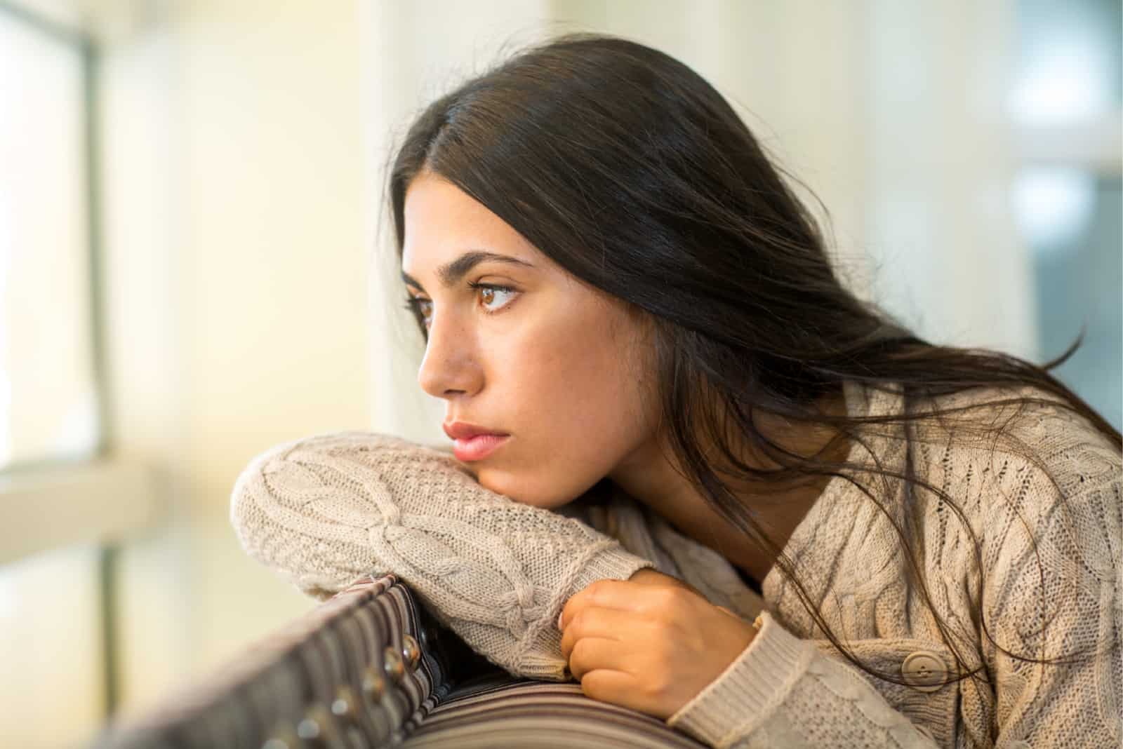 pensive woman in beige sweater looking through window