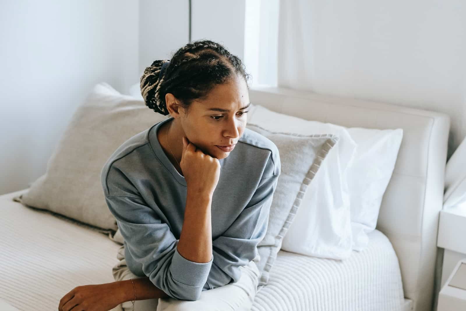 mujer triste con sudadera azul sentada en la cama