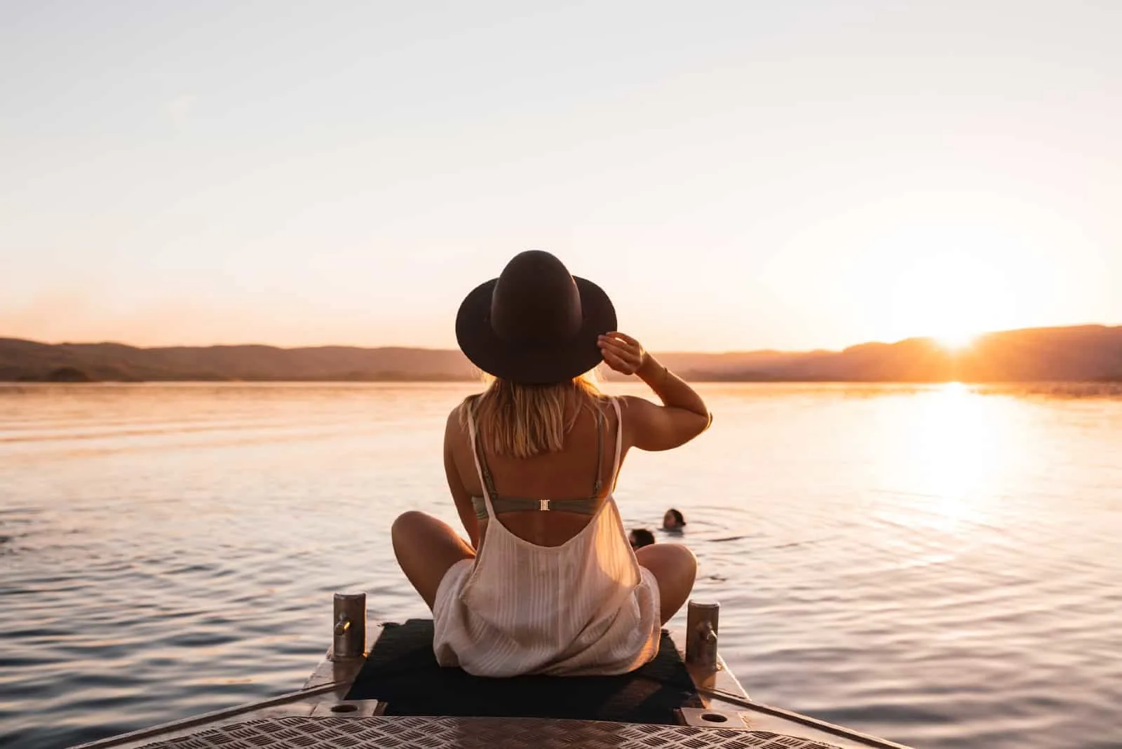 woman sitting on dock looking at water during sunset