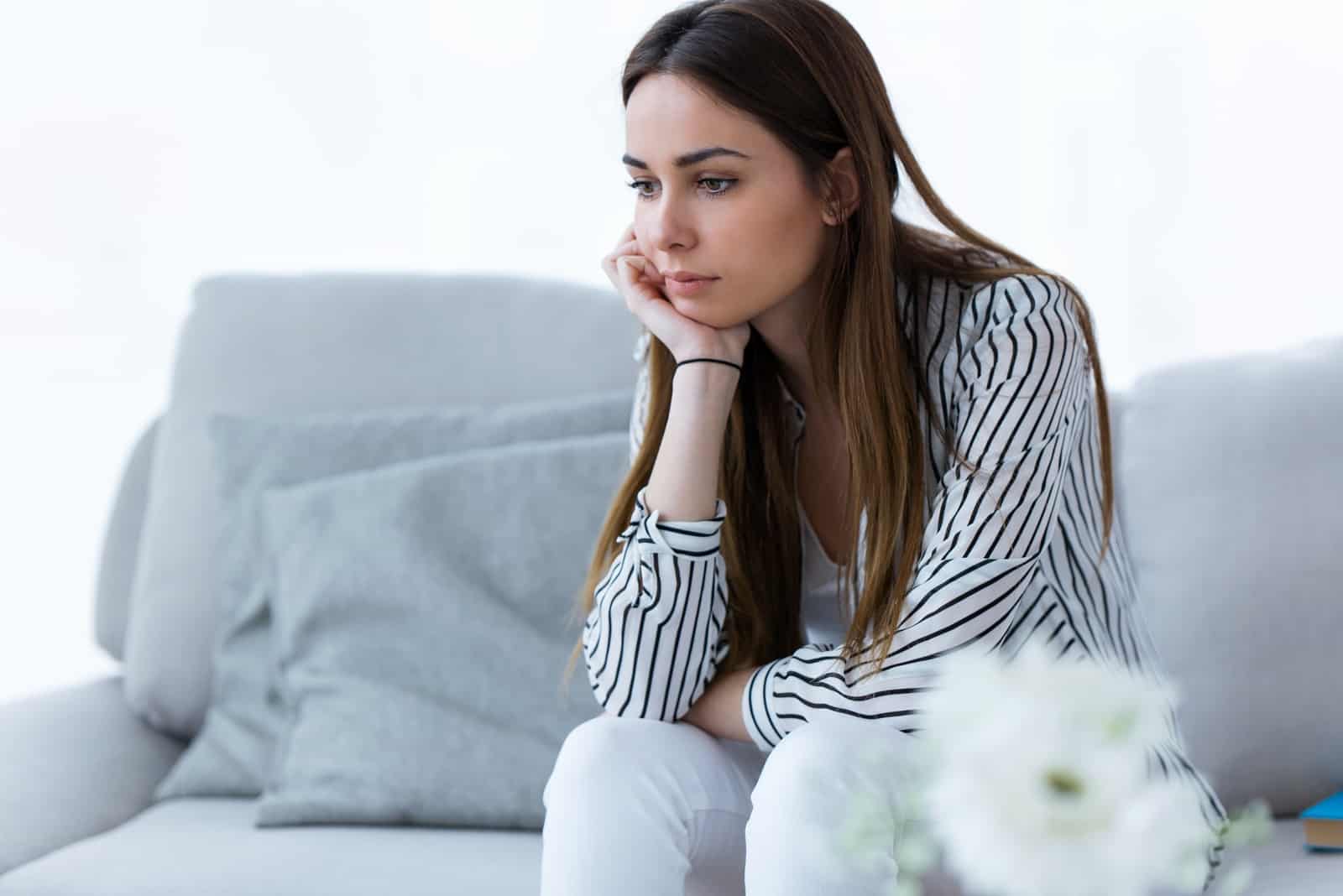 mulher triste com camisa às riscas sentada no sofá