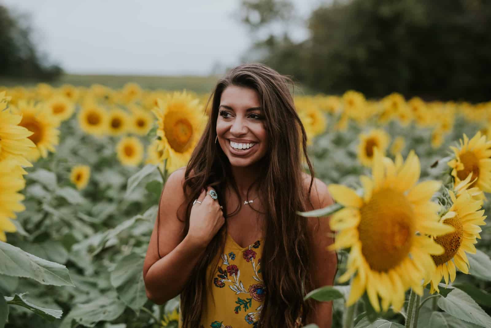 mujer feliz con vestido amarillo de pie en un campo de girasoles