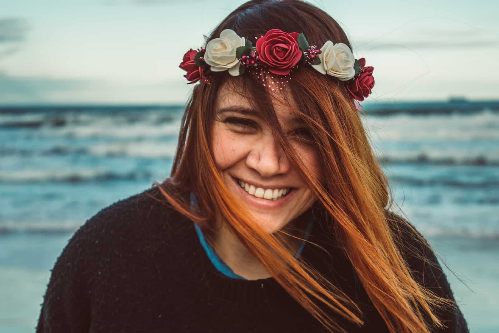 woman with flower crown smiling while standing near sea
