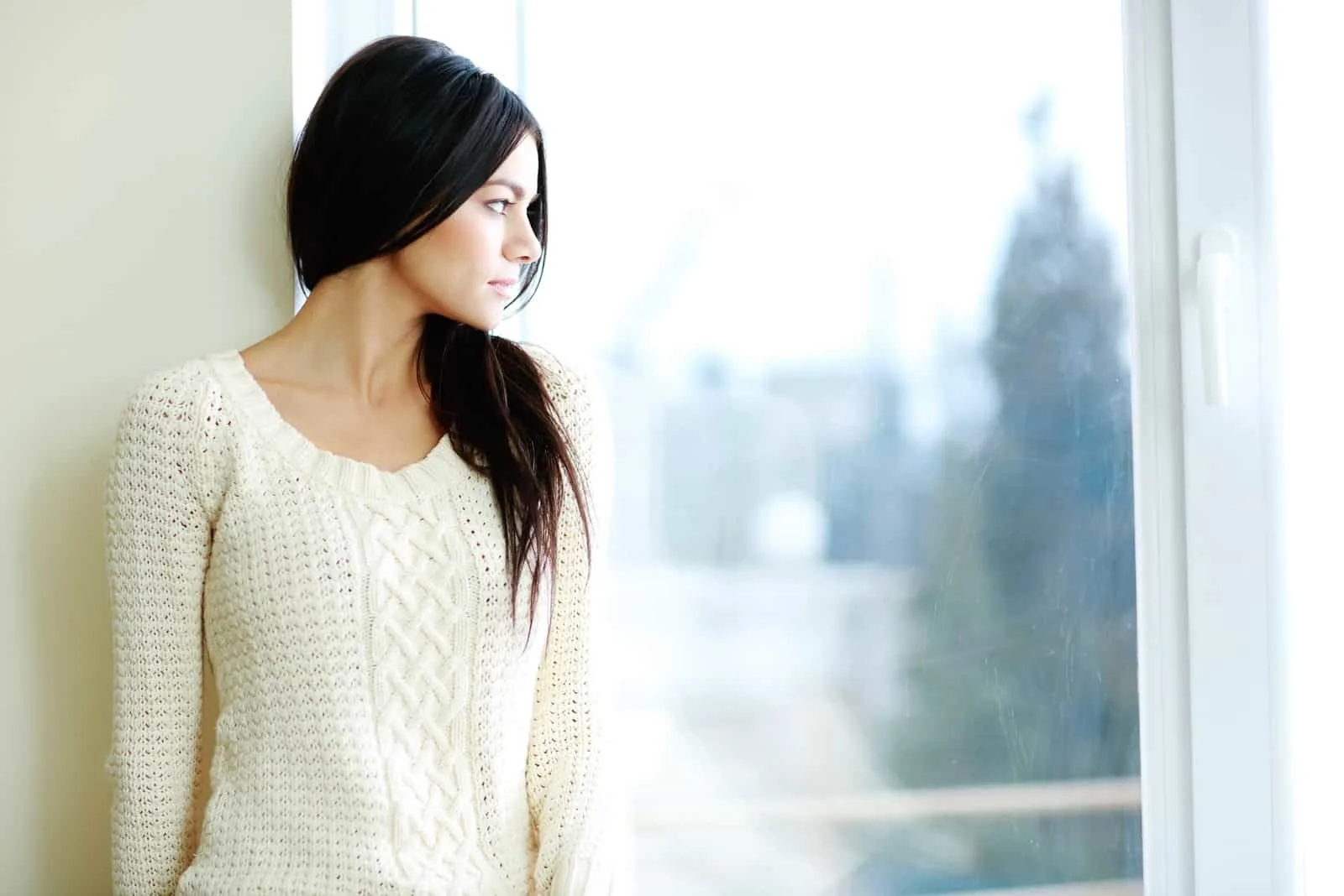 woman in white sweater standing near window