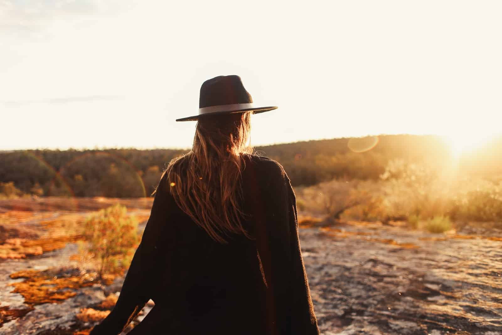 mujer con sombrero de pie sobre las rocas durante la puesta de sol