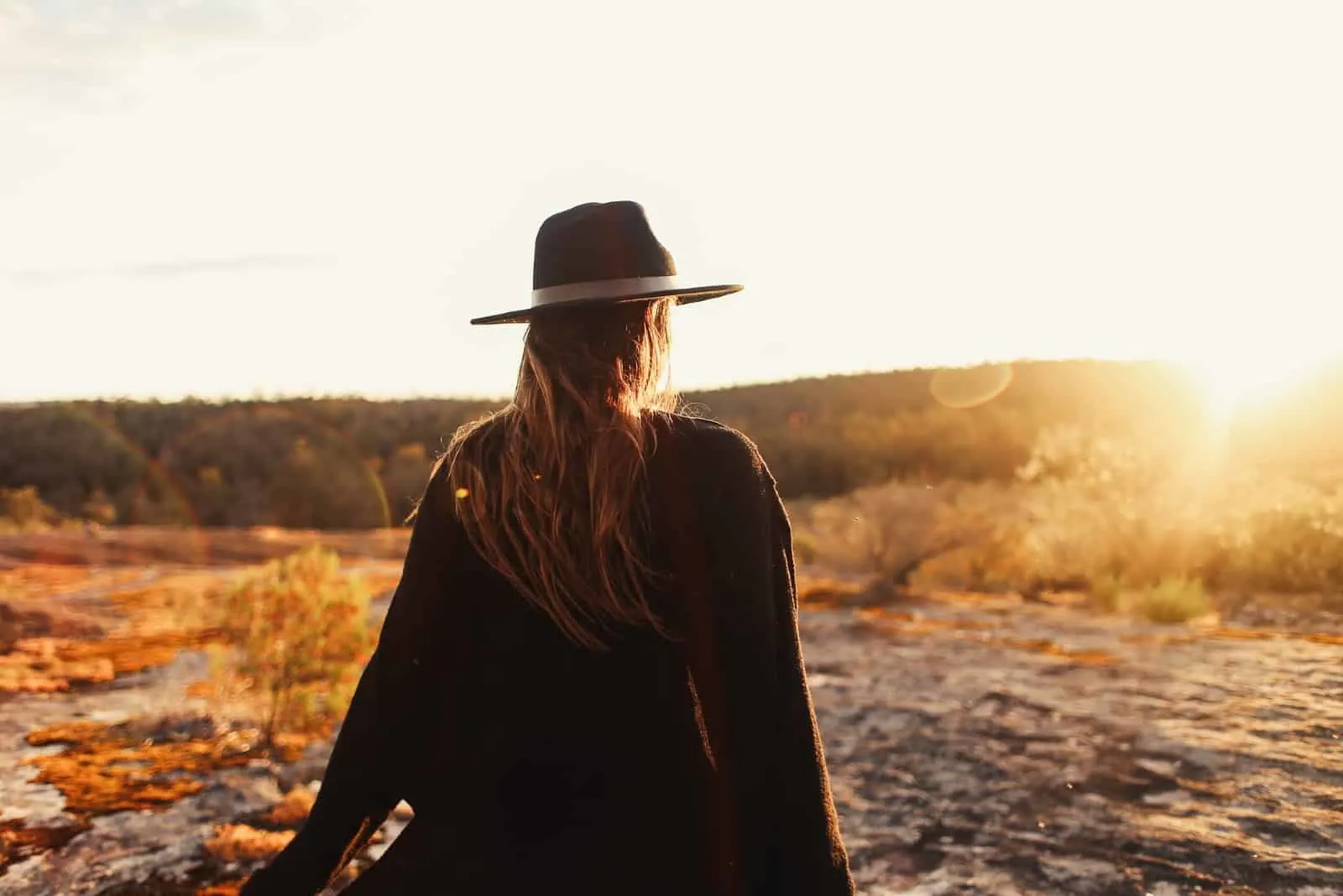 woman with hat standing on rocks during sunset