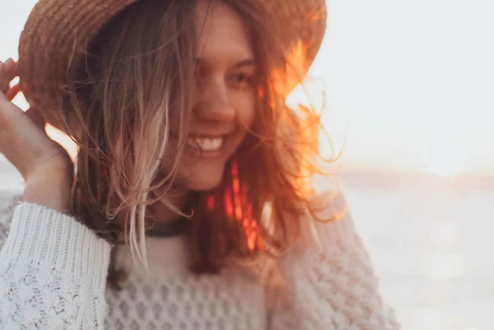 woman in white sweater smiling while touching her hat