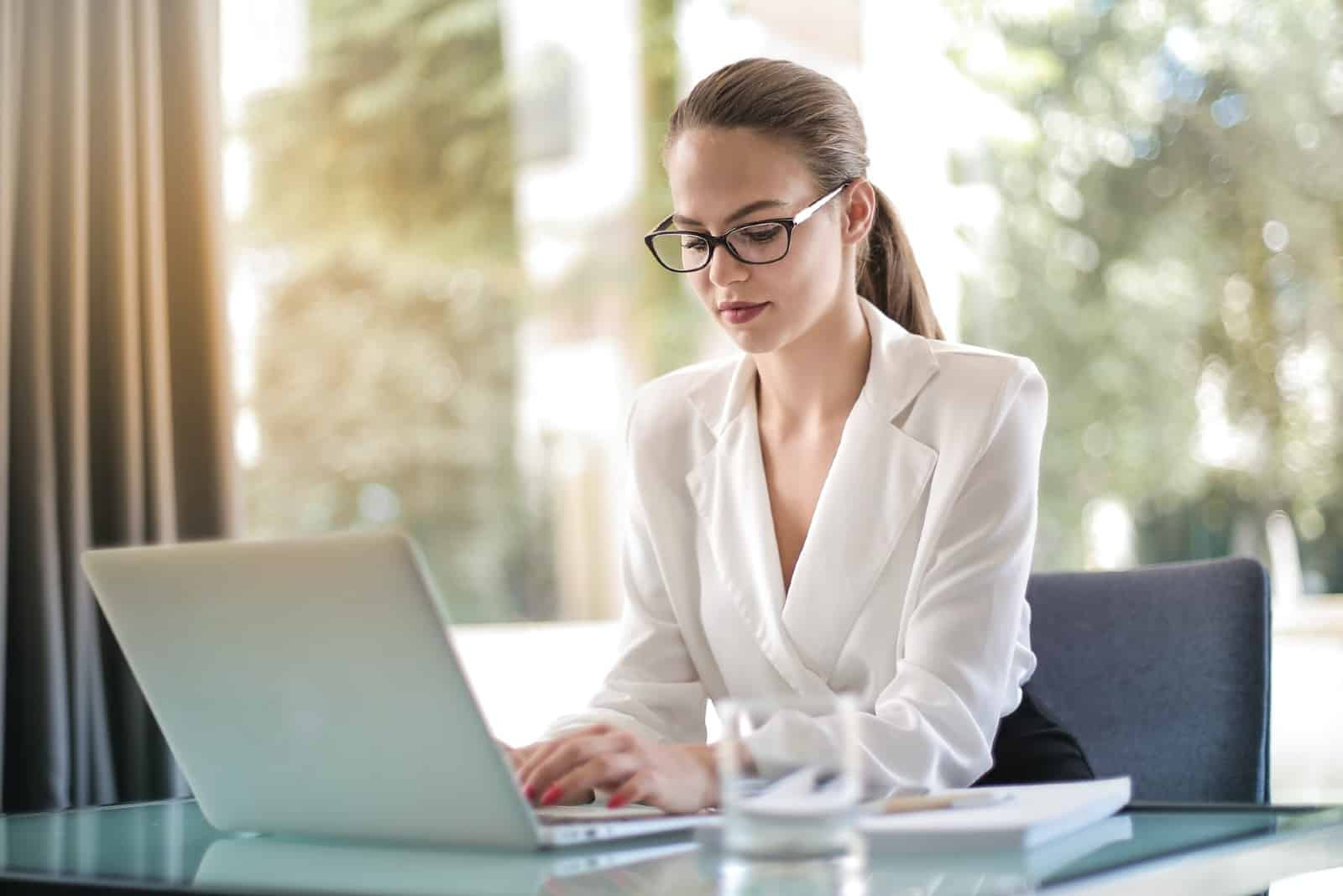 mulher de blusa branca a utilizar um computador portátil enquanto está sentada à mesa