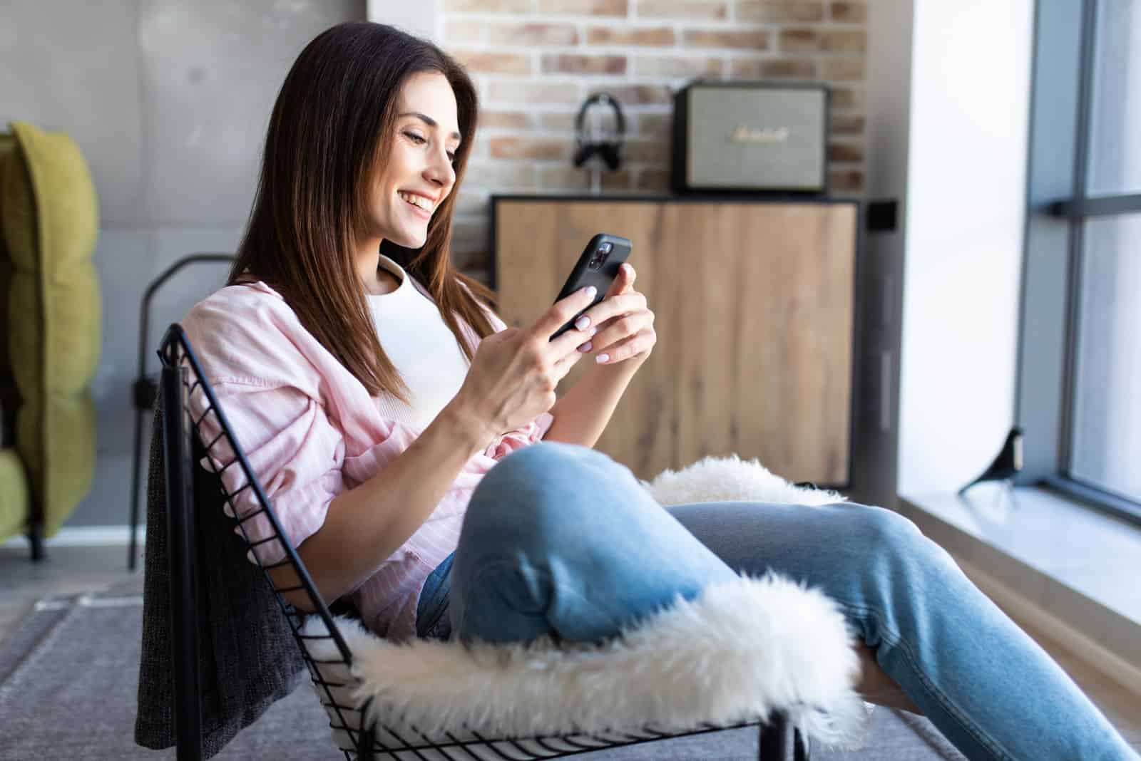 mulher feliz a utilizar o smartphone enquanto está sentada numa cadeira