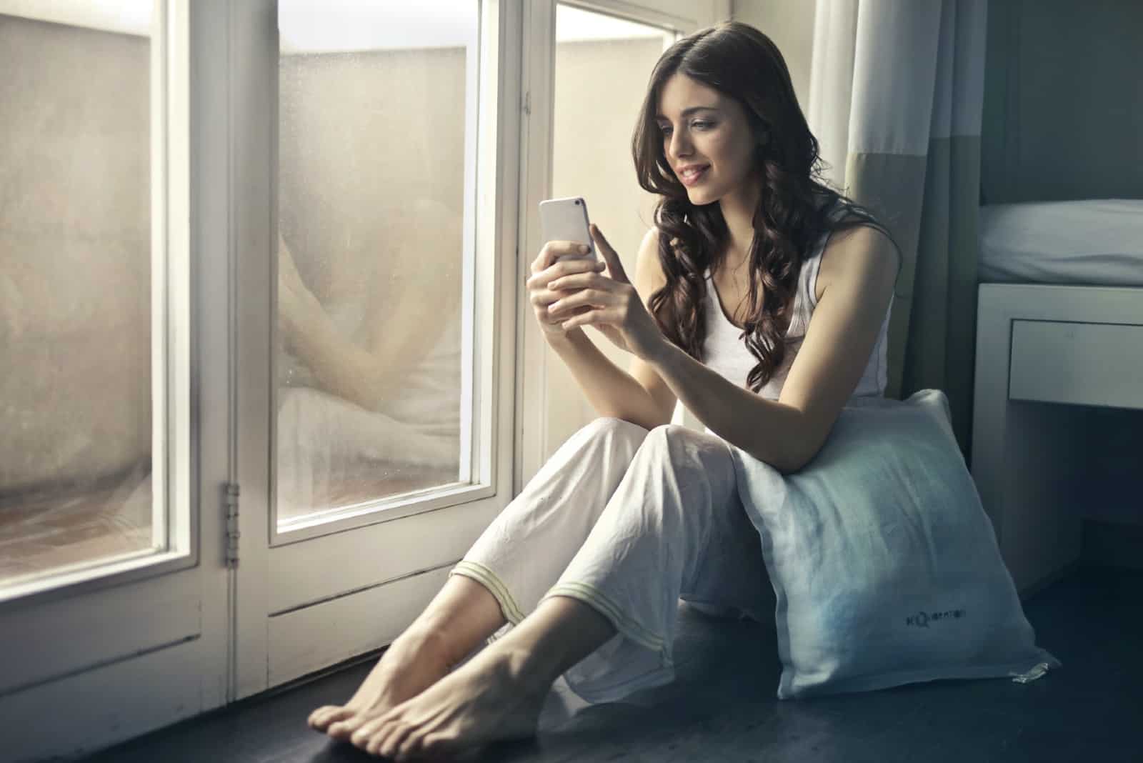happy woman using smartphone while sitting near window